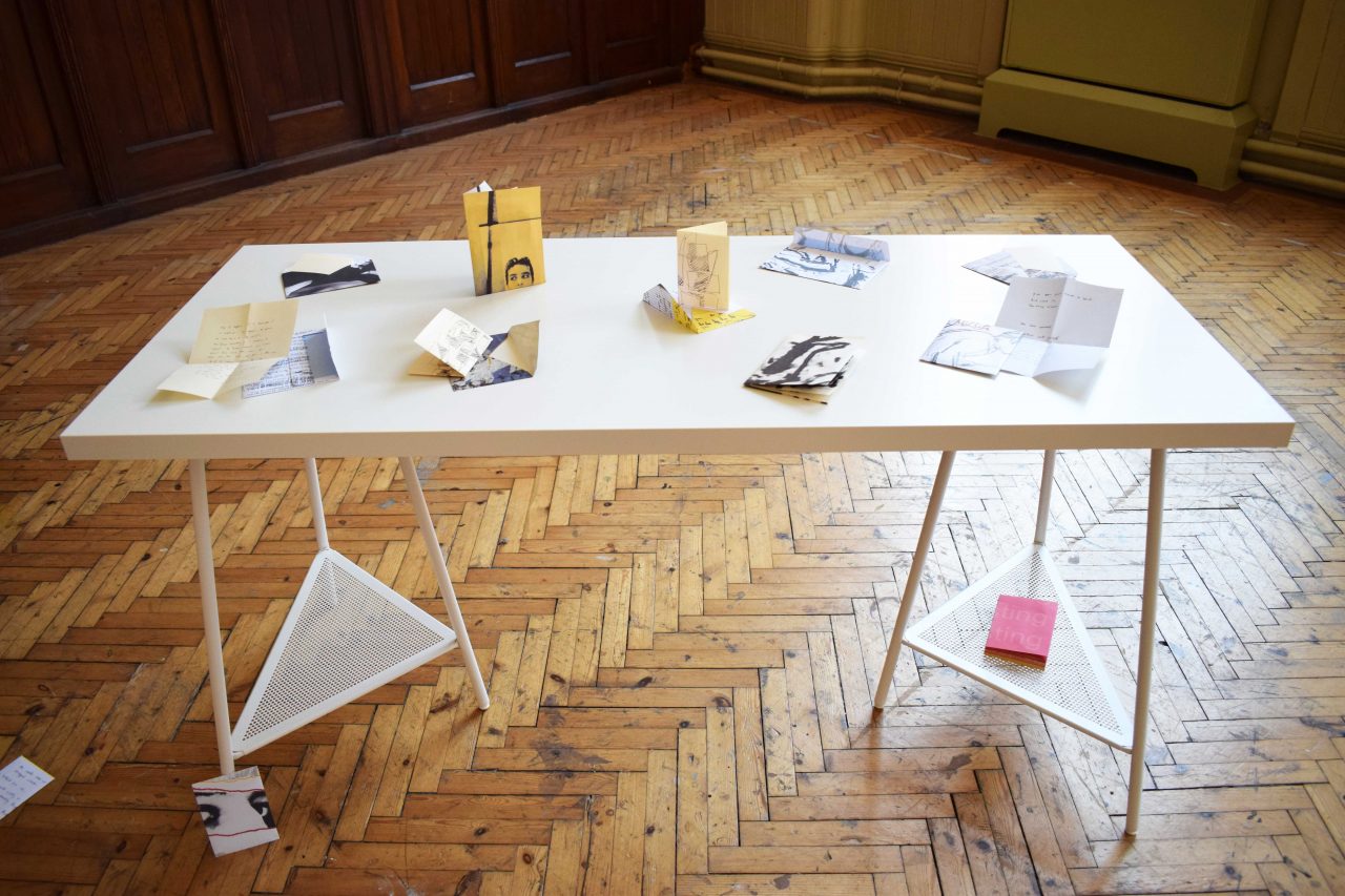 Laid out letter of I Installation of books, letters, and envelopes into space, supported by a table and surrounding wall.