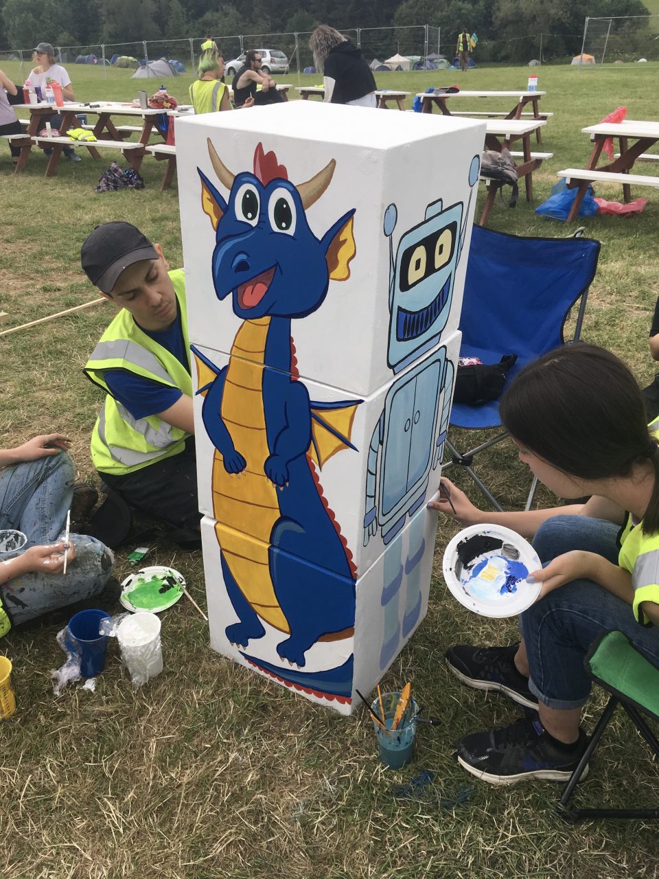 Photograph of three white cubes stacked on top of one another with a cartoon blue and yellow dragon painted on one side.